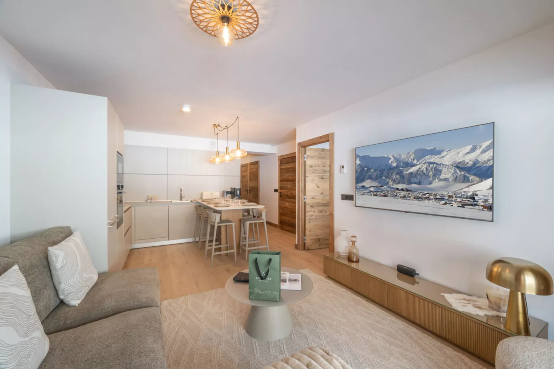 A bright living room opens onto a compact kitchen, with a mountain picture on the wall.
