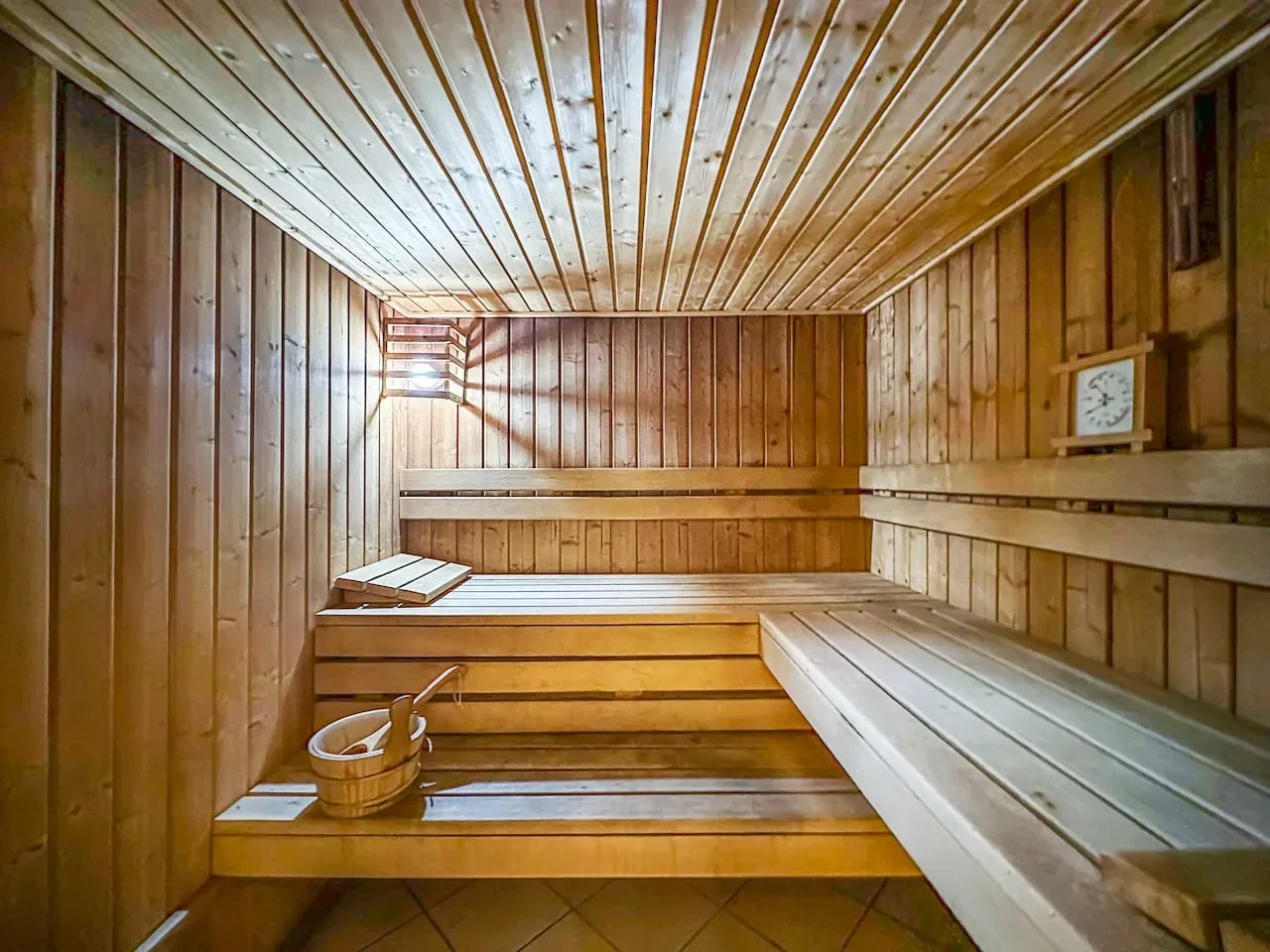 Sauna revestida de madera con asientos escalonados y un pequeño reloj.