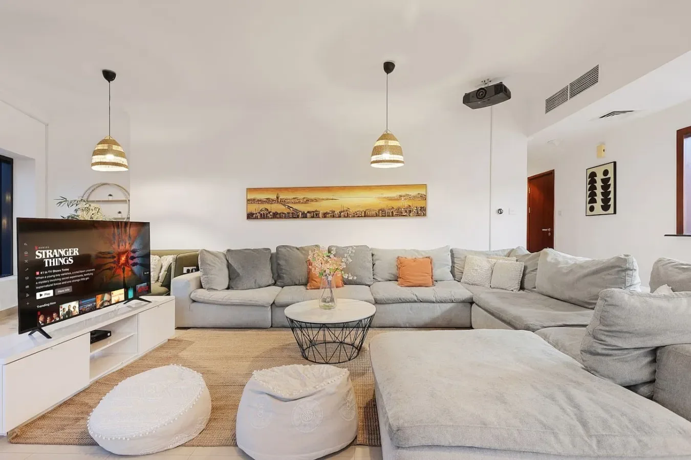 Una sala luminosa con asientos seccionales, un televisor y lámparas colgantes.