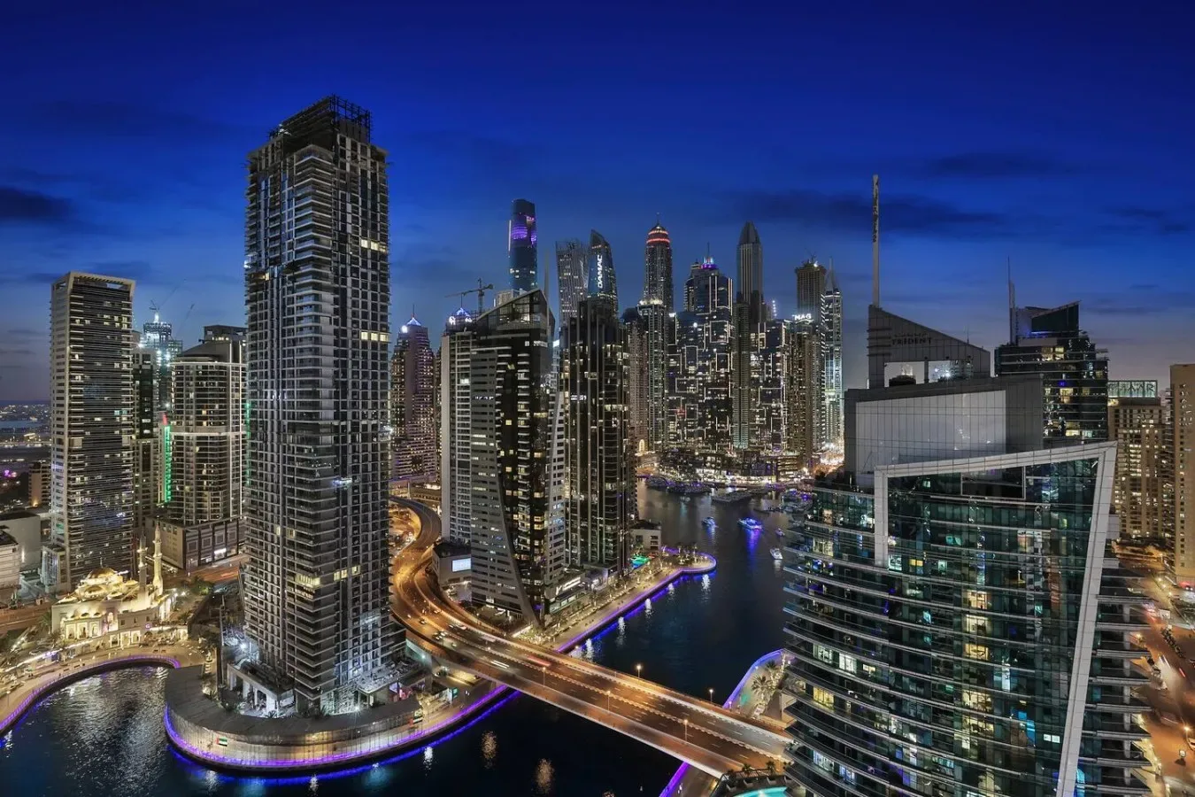 Un horizonte urbano nocturno con edificios altos iluminados junto a un canal sinuoso.