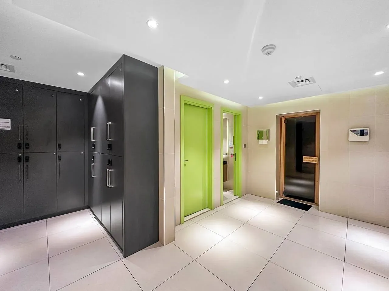 Un pasillo interior con suelo de baldosas, armarios oscuros y una puerta verde brillante.