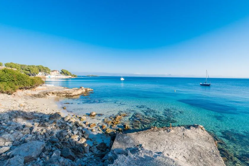 Una costa rocosa se encuentra con aguas azules y claras bajo un cielo despejado.