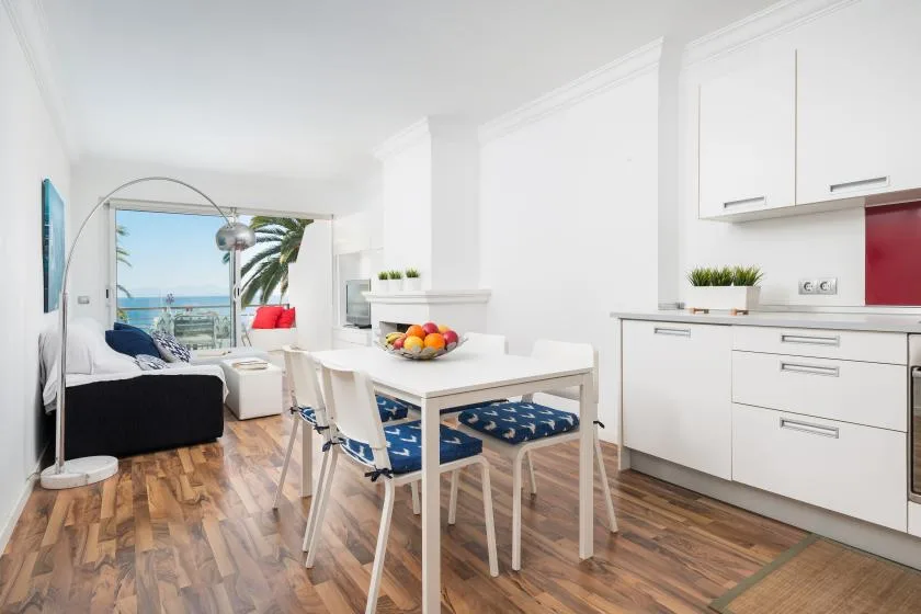 Sala y comedor de concepto abierto con una mesa blanca junto a una cocina compacta.