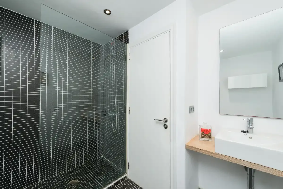 Un baño con una ducha de azulejos oscuros y un lavabo con mueble.
