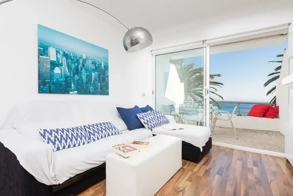 Una sala luminosa con asientos blancos y puertas corredizas de vidrio que dan a una terraza.