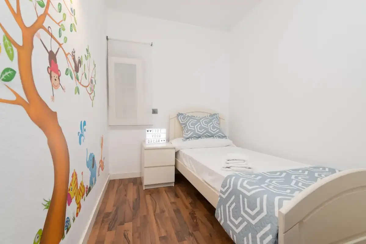 Un dormitorio infantil con una cama individual y un mural colorido de un árbol.