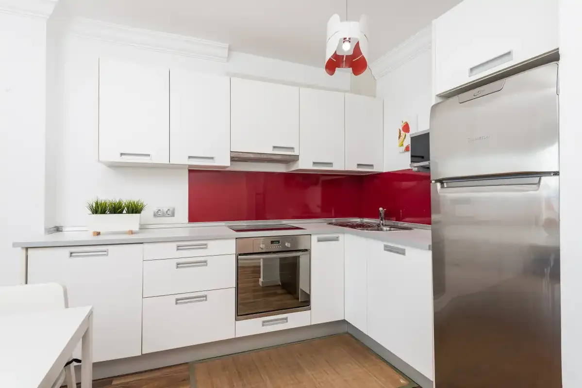Una cocina moderna con armarios blancos y un salpicadero rojo.
