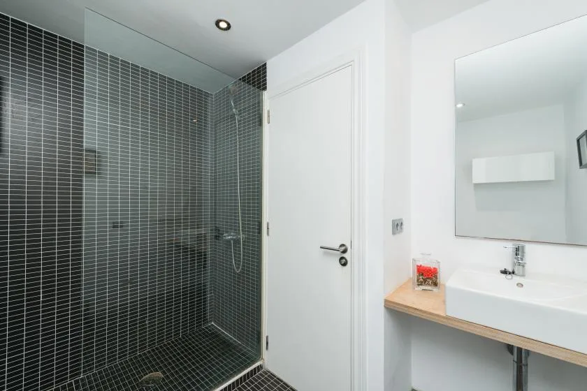 Un baño moderno con una ducha de azulejos oscuros y un lavabo blanco.