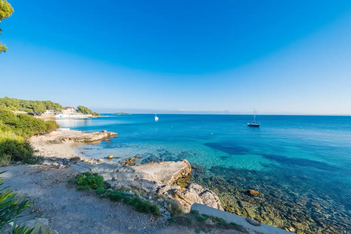 Una costa rocosa se encuentra con aguas azules y claras bajo un cielo luminoso.