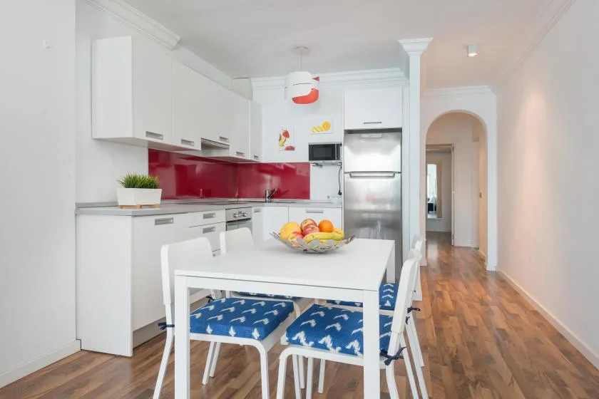 Una cocina y comedor luminosos con una mesa blanca y asientos azules estampados.