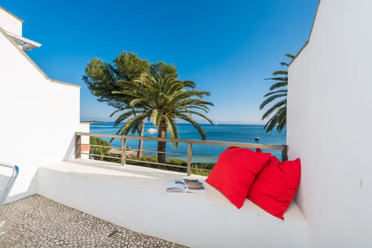Una terraza frente al mar tiene cojines rojos, palmeras y vistas al agua.