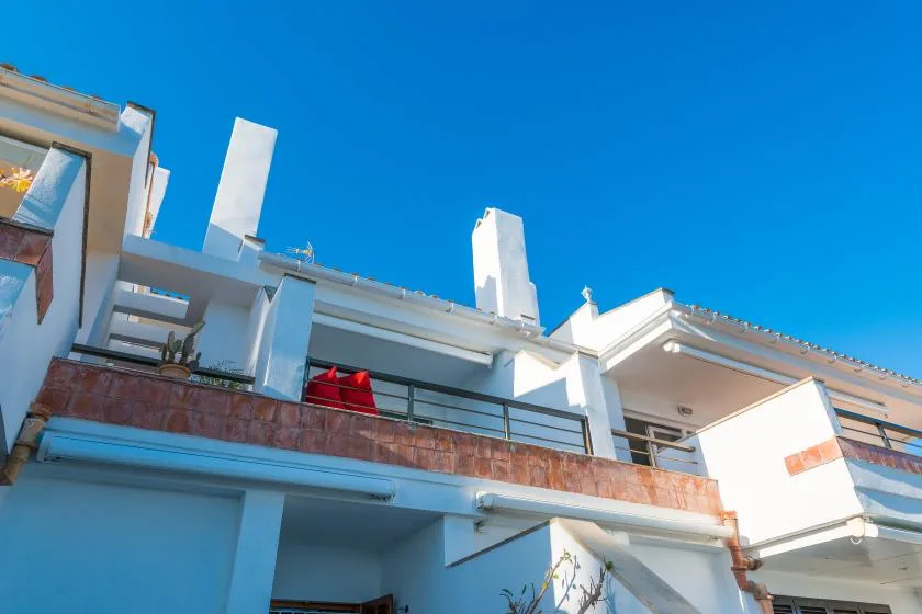 Un edificio blanco de varias plantas con balcones se alza bajo un cielo azul despejado.