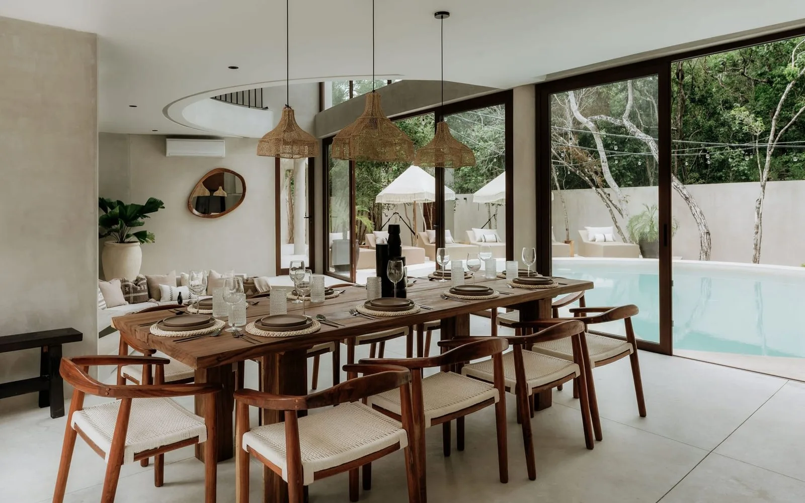 A dining area with a long wooden table set beside floor-to-ceiling windows.