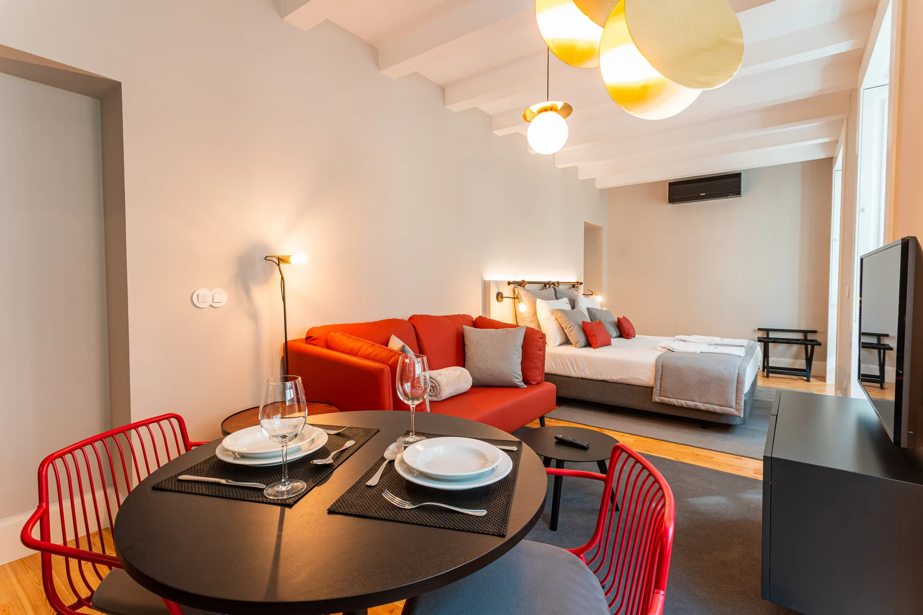 Un estudio combina una zona de comedor con asientos rojos y una cama.