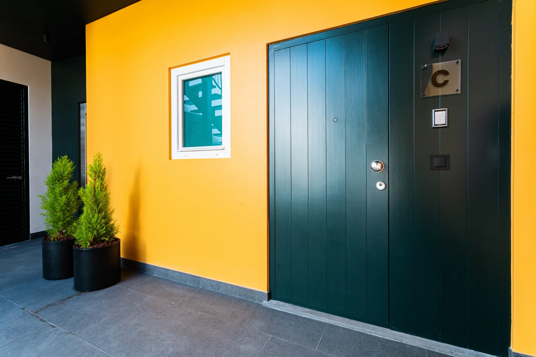 A yellow exterior wall with a dark teal entrance door and potted plants.