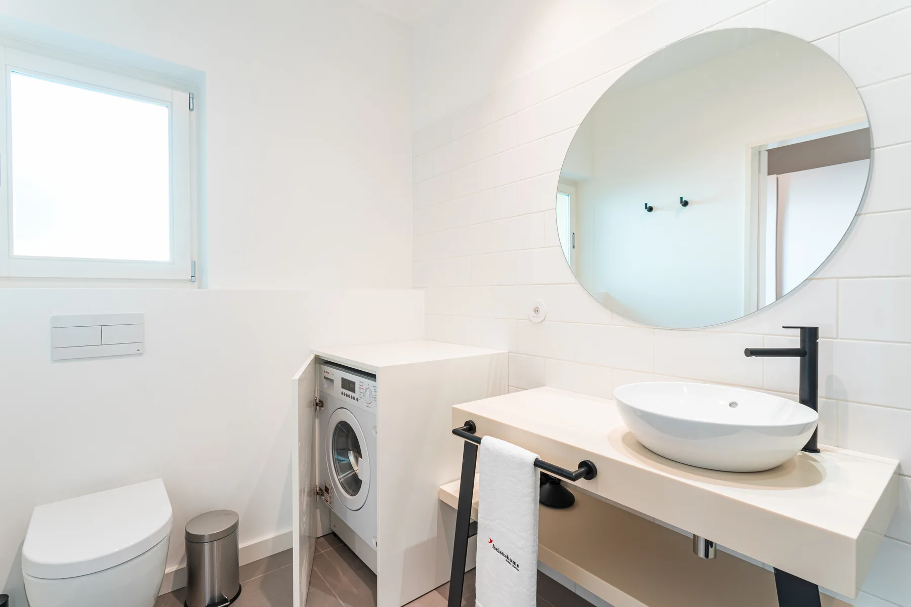 A bright bathroom with a washing machine beside the sink and toilet.