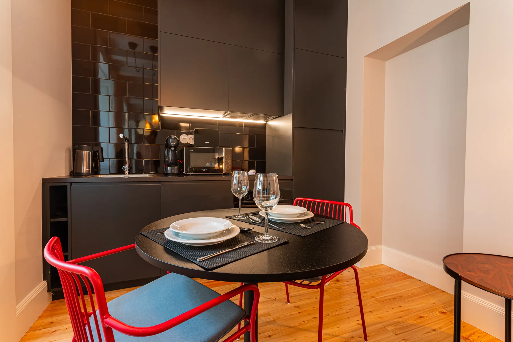 Un comedor con una mesa redonda y sillas rojas está junto a una cocina compacta.