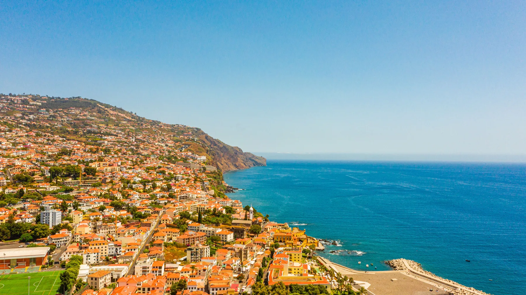 Una ciudad costera se extiende por una ladera junto al océano azul.