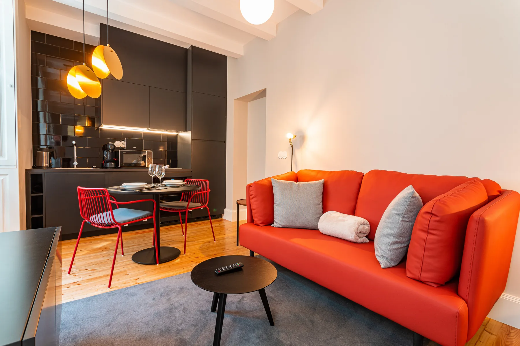 Una sala de estar tipo estudio con asientos naranjas junto a una mesa de comedor.