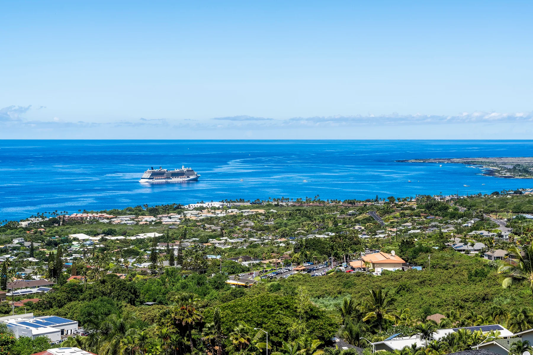 Paisaje costero con un crucero en el mar azul, más allá de una costa verde y urbanizada.