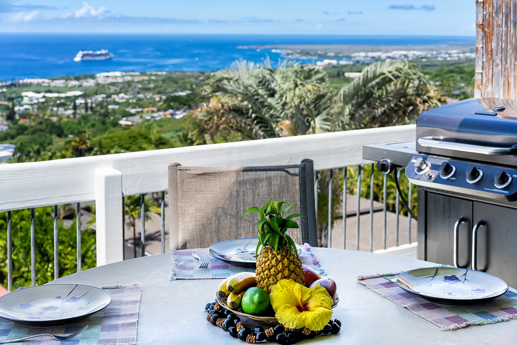 Una zona de comedor en el balcón da al océano, con fruta en una mesa y una parrilla cerca.
