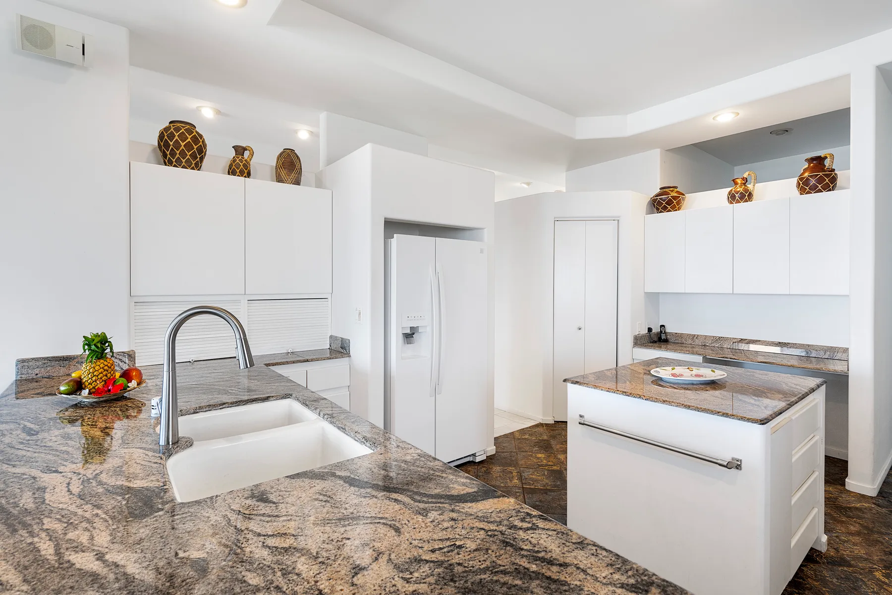 Una cocina moderna y luminosa tiene gabinetes blancos, encimeras de piedra y una isla central.