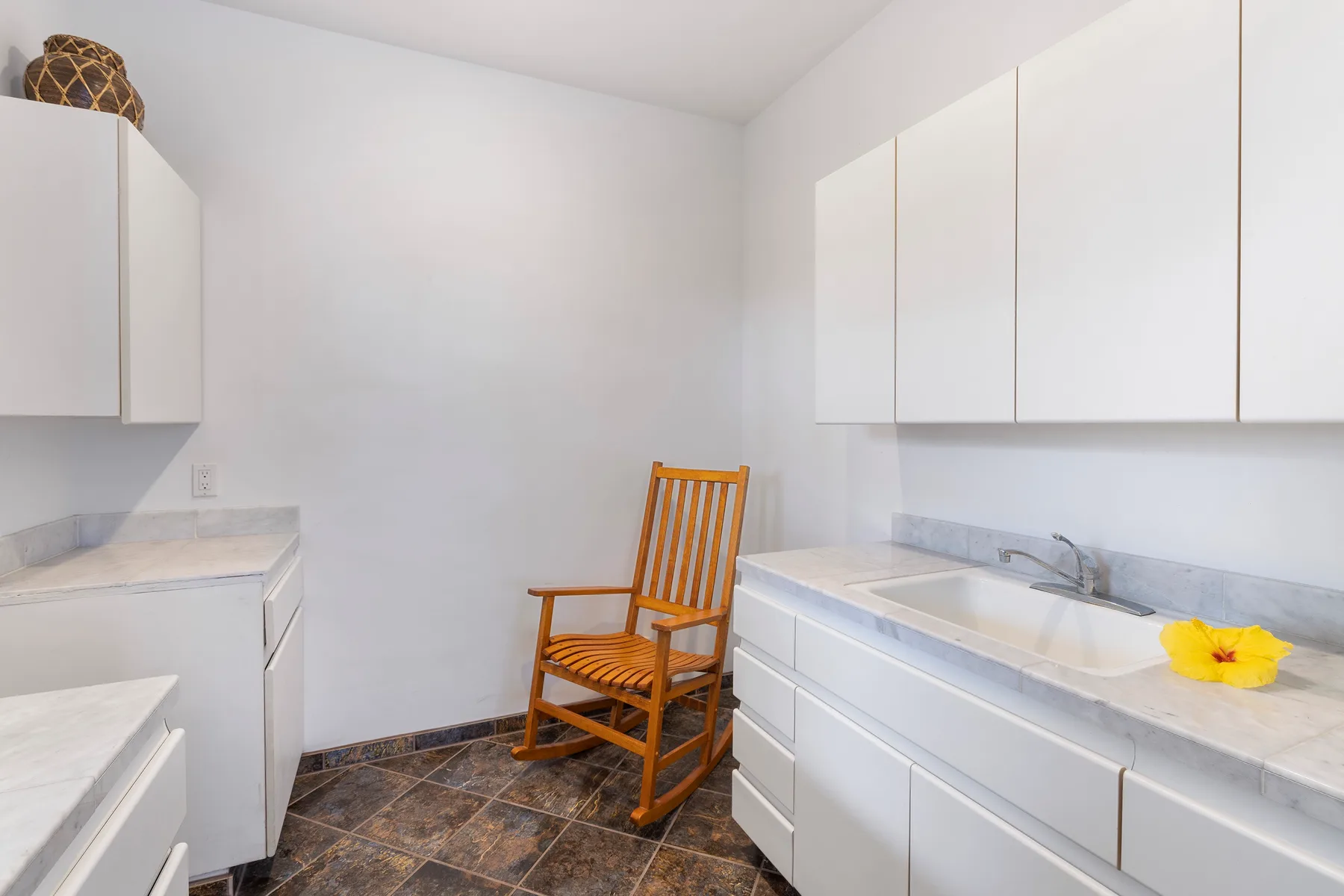 Un baño luminoso con una silla de madera entre dos encimeras blancas.