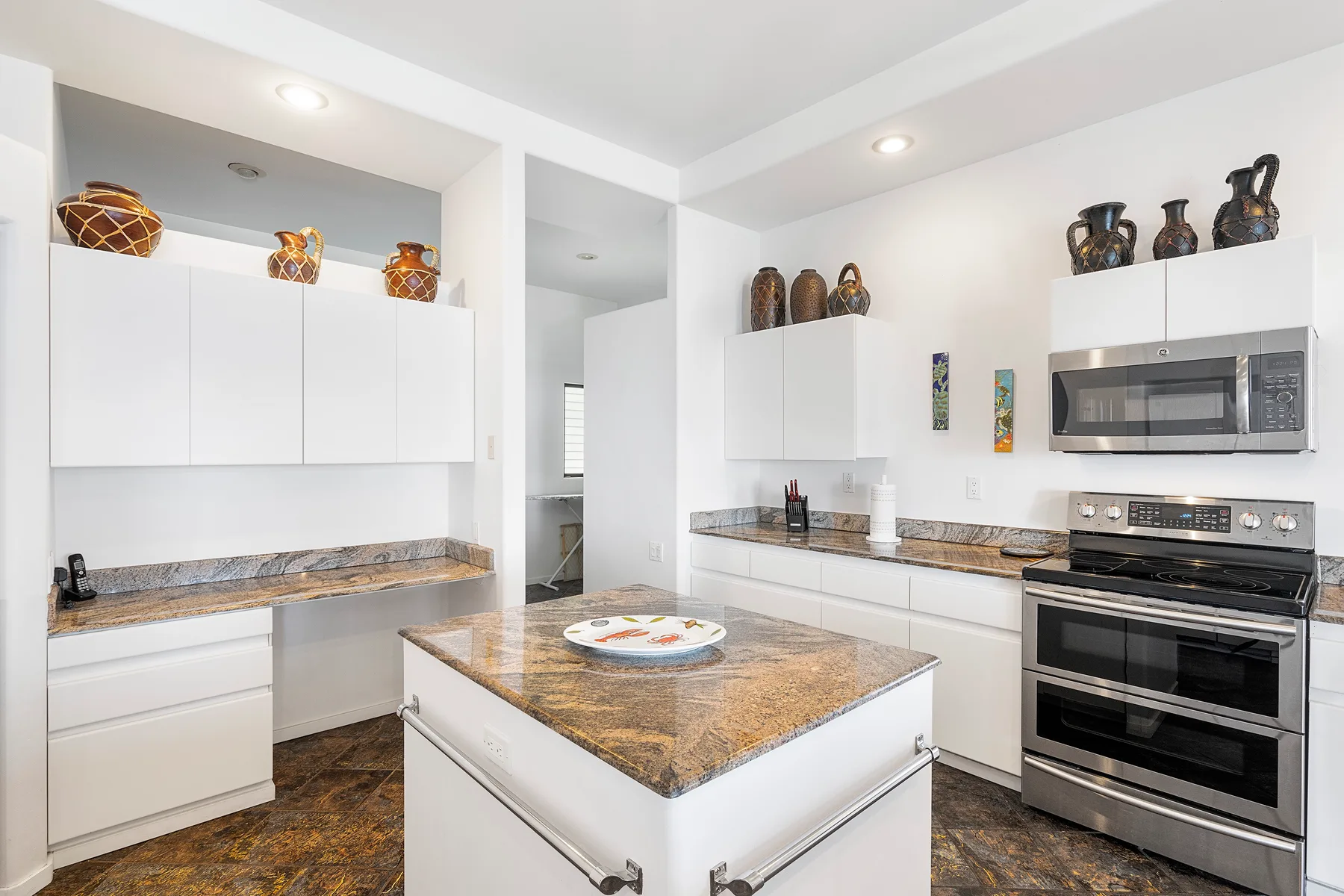 Una cocina blanca y luminosa con una isla central y electrodomésticos de cocción integrados.