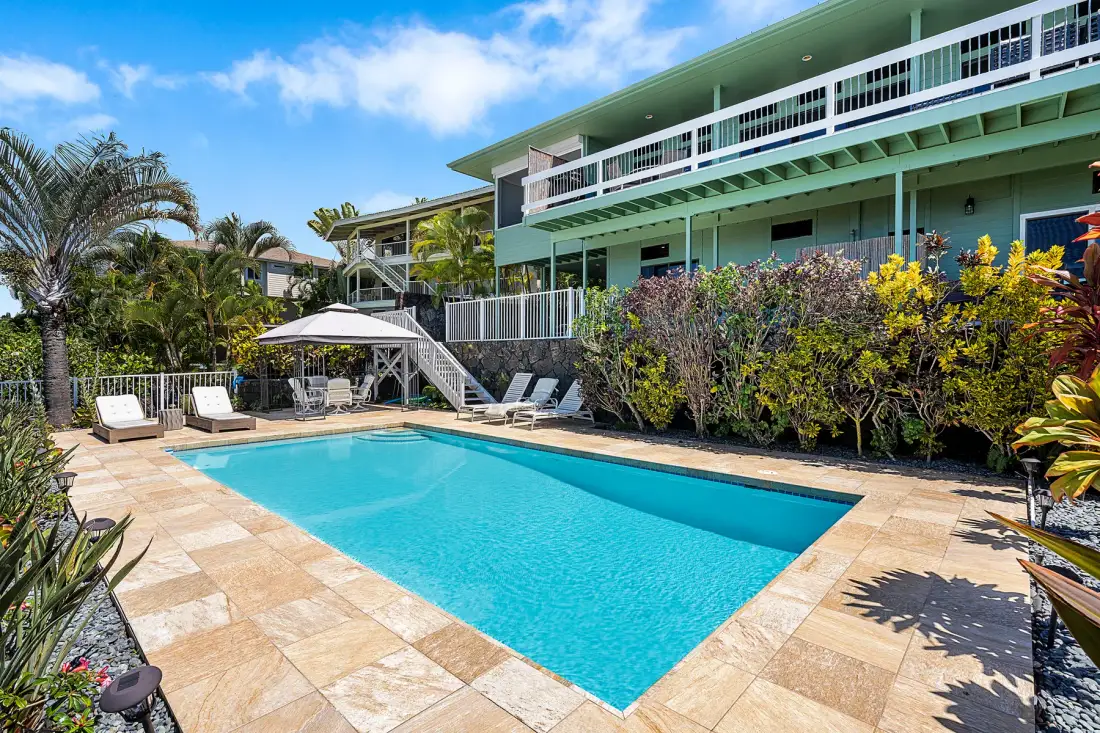 Una piscina exterior junto a un edificio de varias plantas y un patio ajardinado.