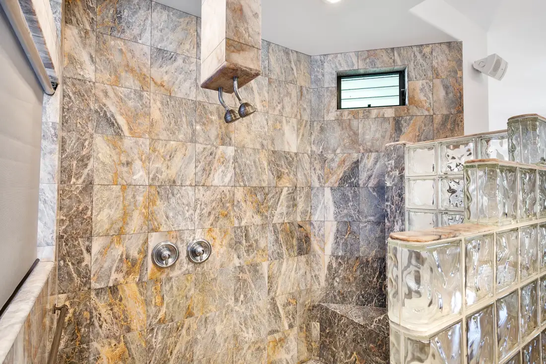 Zona de ducha con azulejos, una ventana alta pequeña y una mampara de bloques de vidrio.