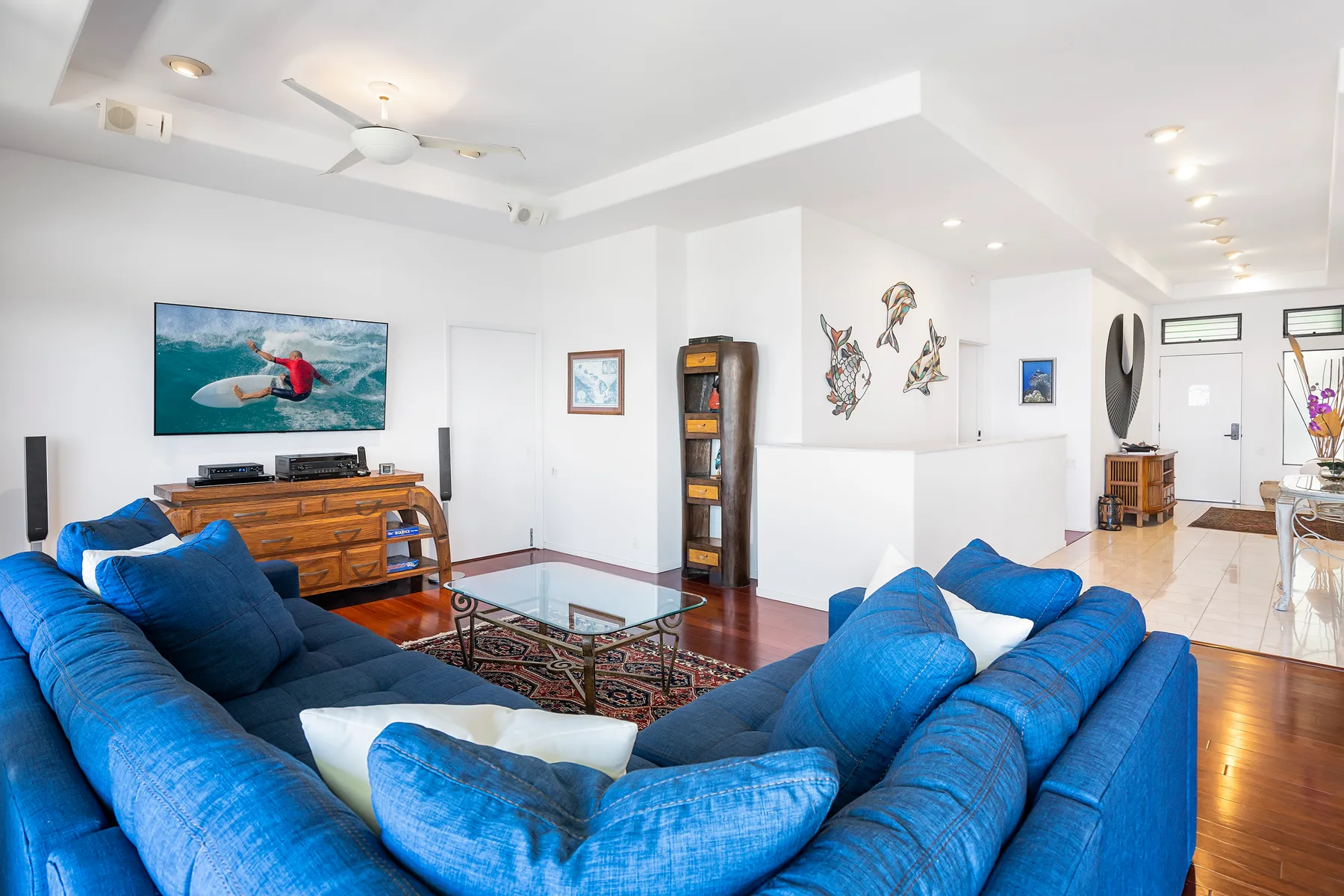 Una sala luminosa con asientos azules, un televisor y una mesa de centro de vidrio.