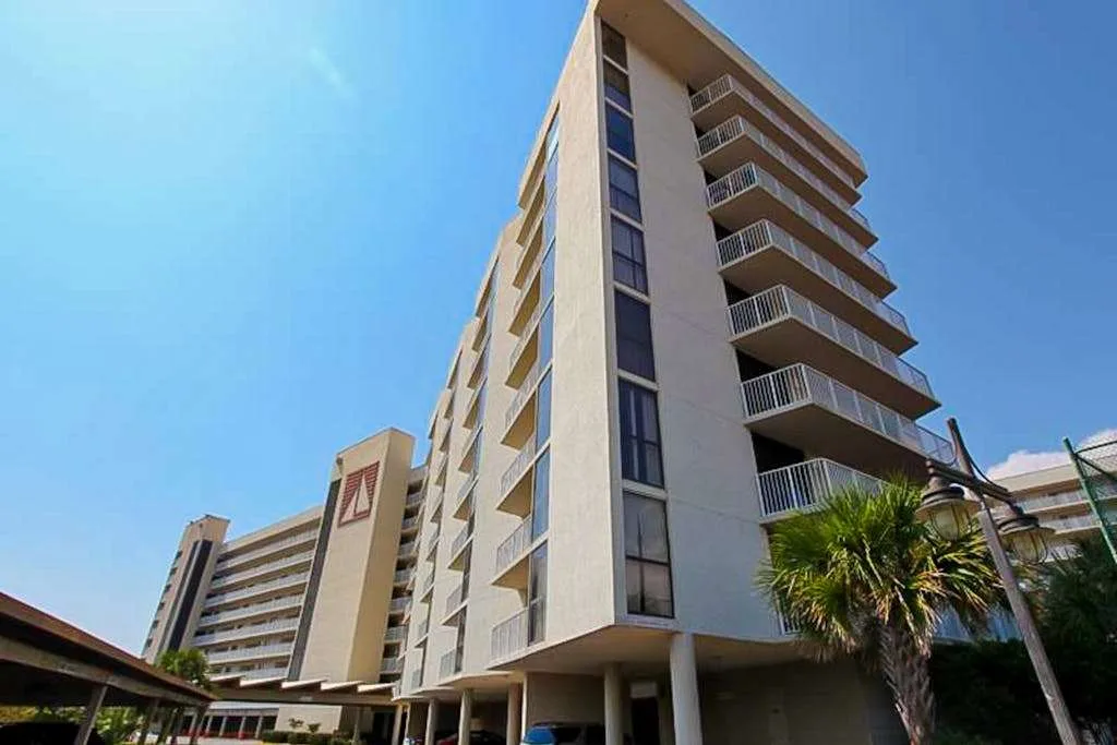 A modern multi-story building with balconies rises beside palm trees under a clear sky.