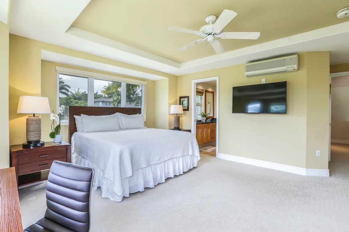 A bright bedroom with a large bed, bedside tables, and a wall-mounted television.