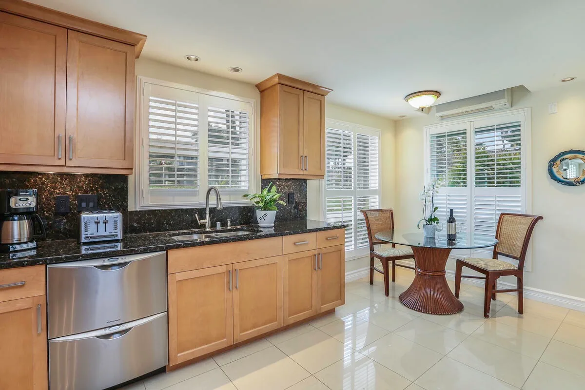 A bright kitchen and dining area with wooden cabinets, a dark countertop, and a round table.