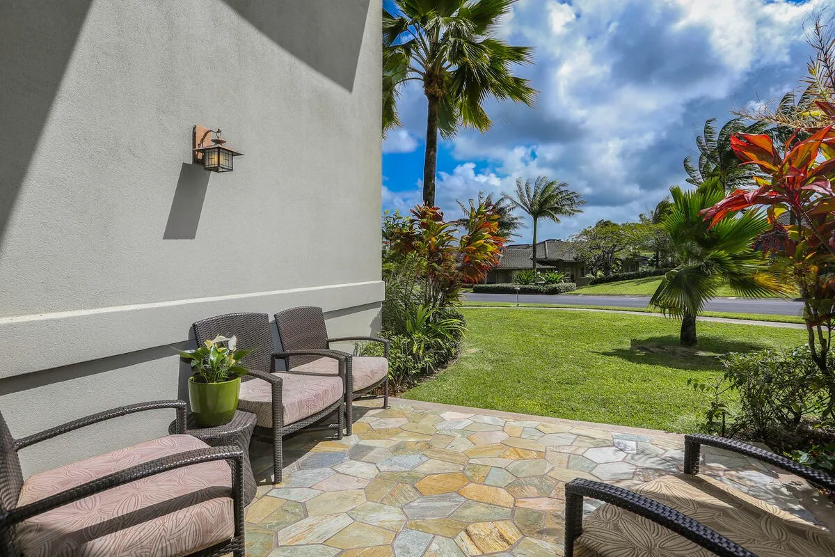 An outdoor patio with cushioned seating overlooks a green lawn and palm trees.