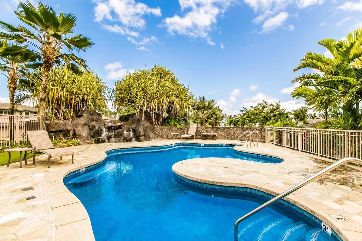 A curved outdoor swimming pool sits among palm trees and tropical landscaping.