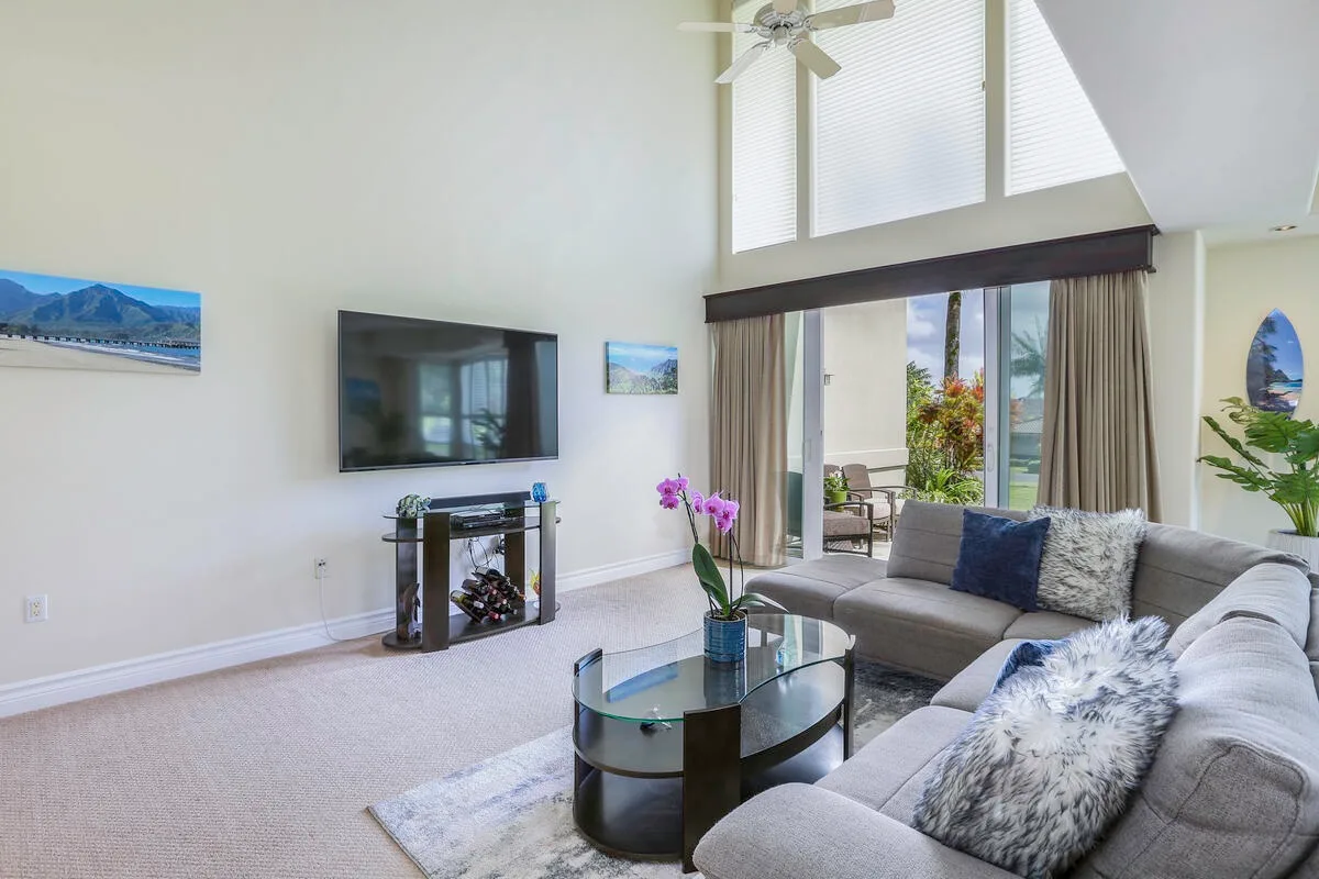 A bright living room with a sectional sofa, glass coffee table, and large windows.