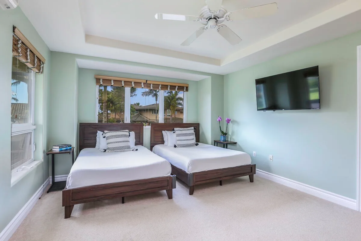 A bedroom with two beds, windows, and a wall-mounted television.