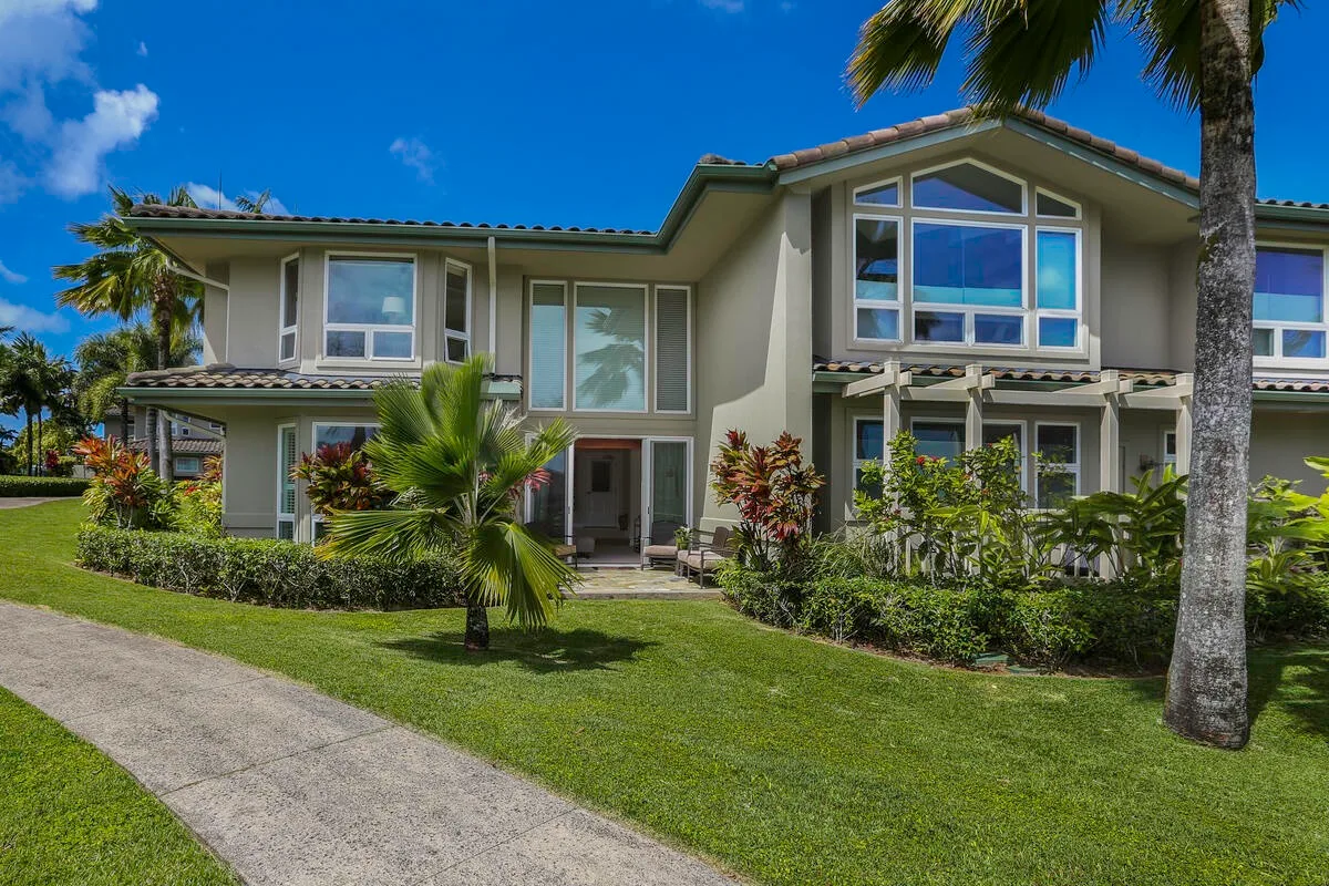 A modern two-story house with large windows, landscaped gardens, and a paved walkway.