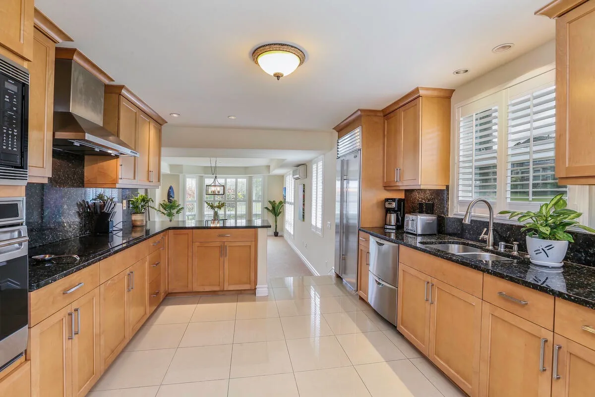 A bright kitchen with wooden cabinetry, dark countertops, and a central tiled walkway.