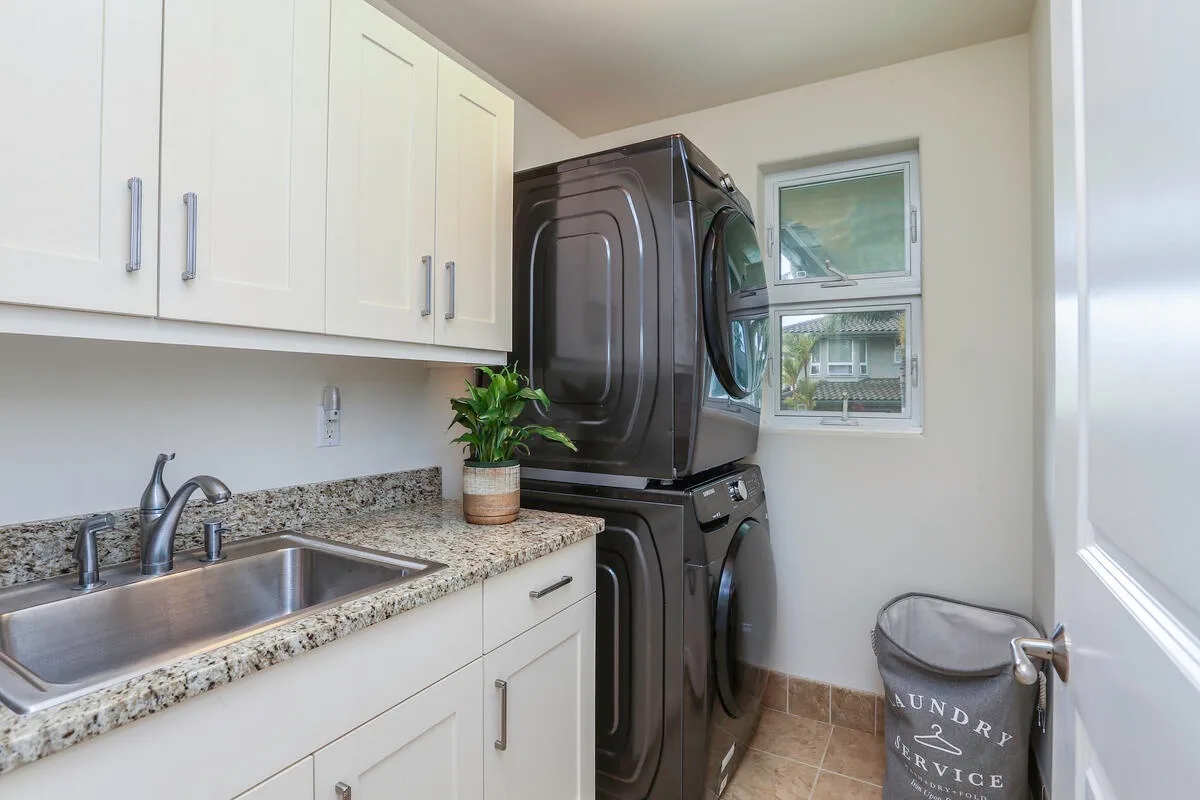A laundry room with stacked laundry machines beside a sink and cabinets.