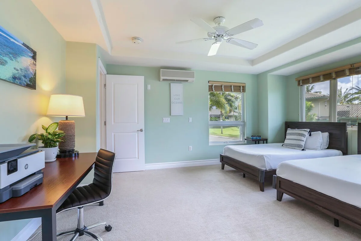 A bright bedroom with two beds, a desk, and windows.