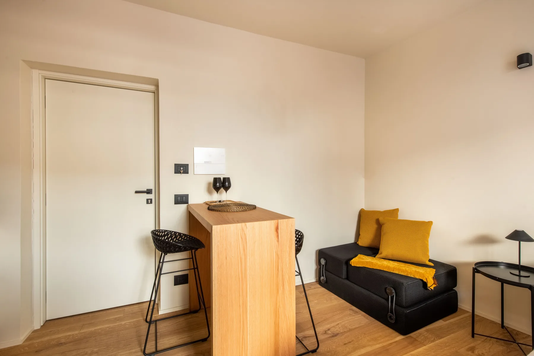 A compact room with a wooden counter, stools, and a black sofa.