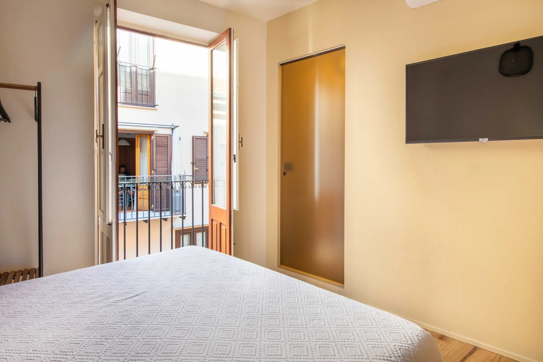 Un dormitorio con una cama, una ventana abierta y un televisor en la pared.