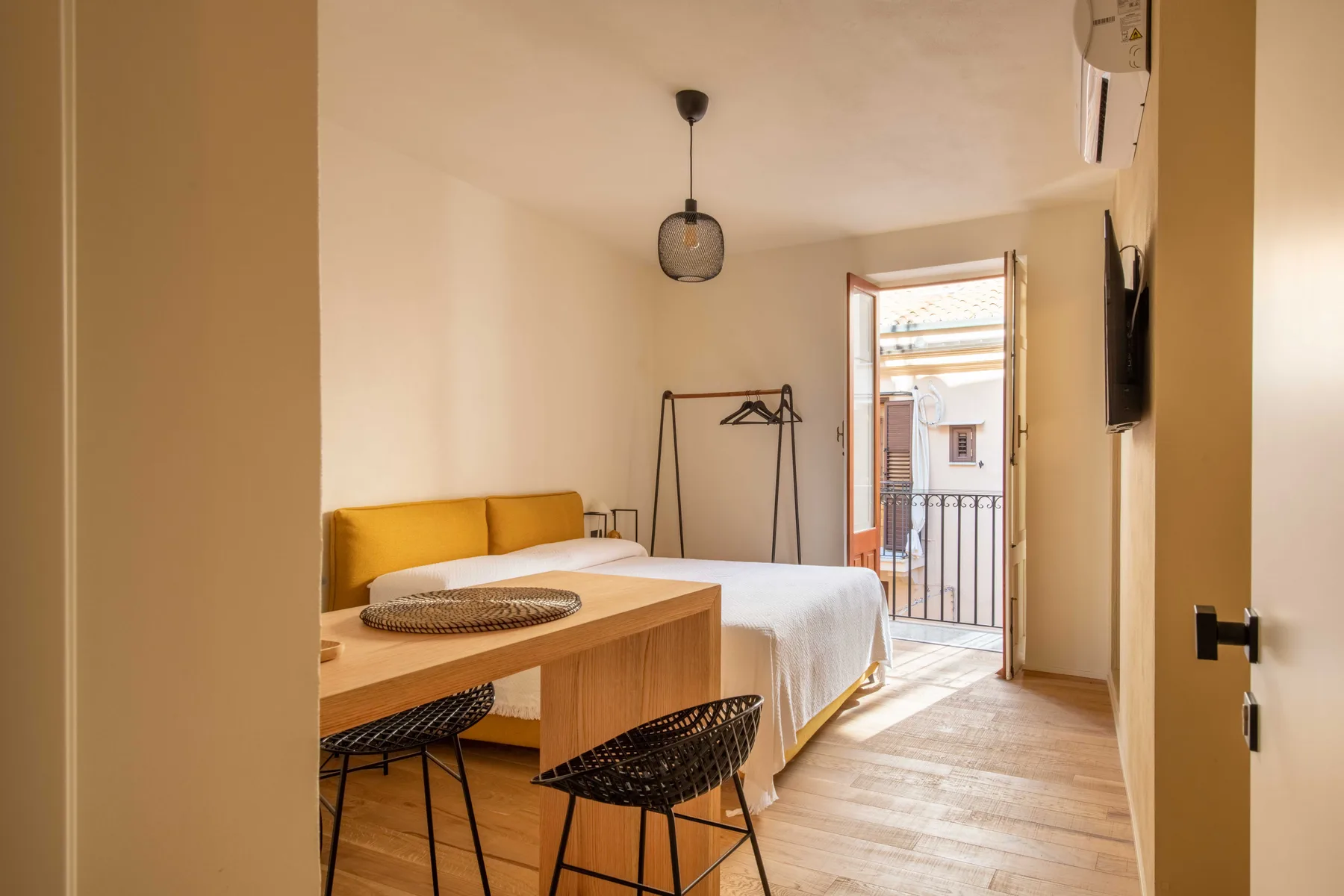 A bedroom with a bed, a wooden table, and an open balcony door.