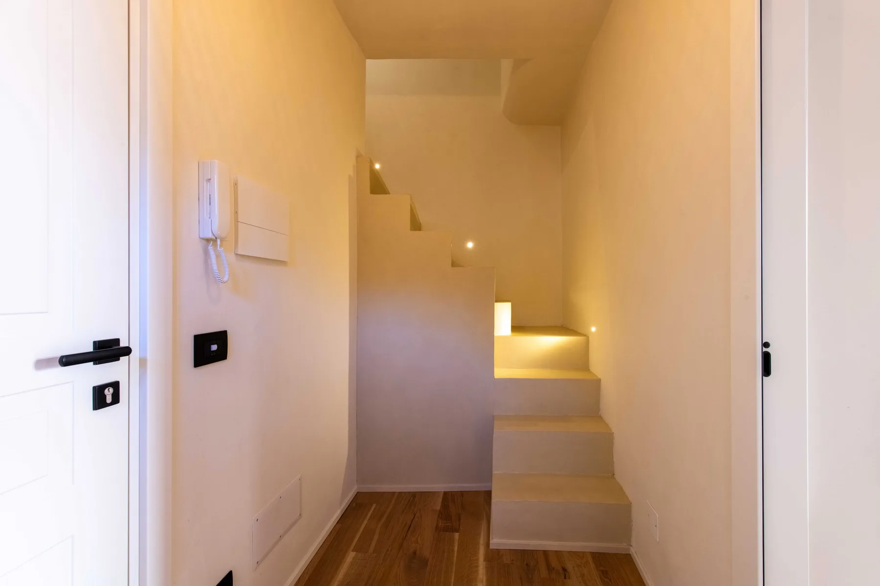 Una escalera interior estrecha con iluminación cálida y suelo de madera.