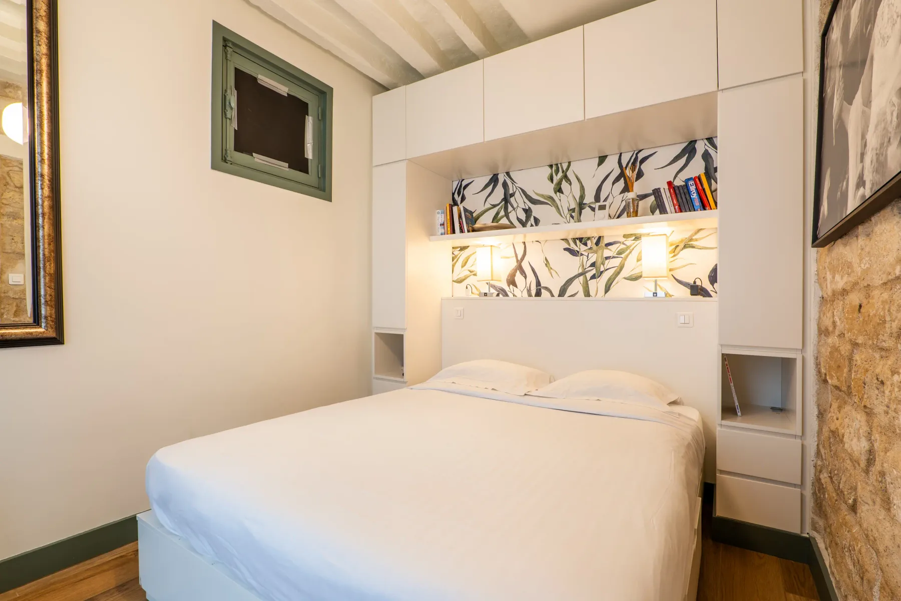 A bedroom with a bed beneath built-in cabinets and a patterned wall panel.