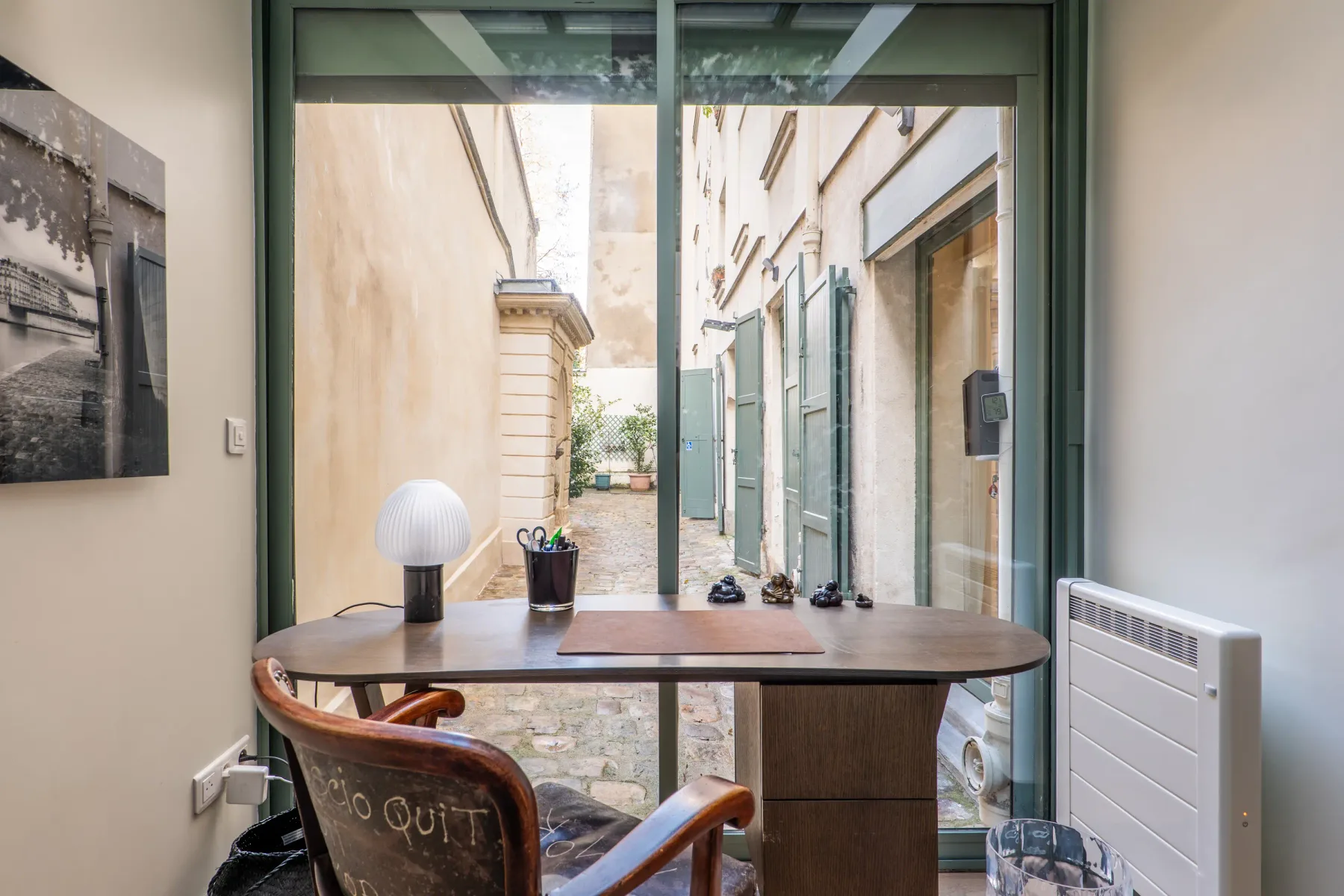 A desk and chair sit beside a large window overlooking a narrow courtyard.