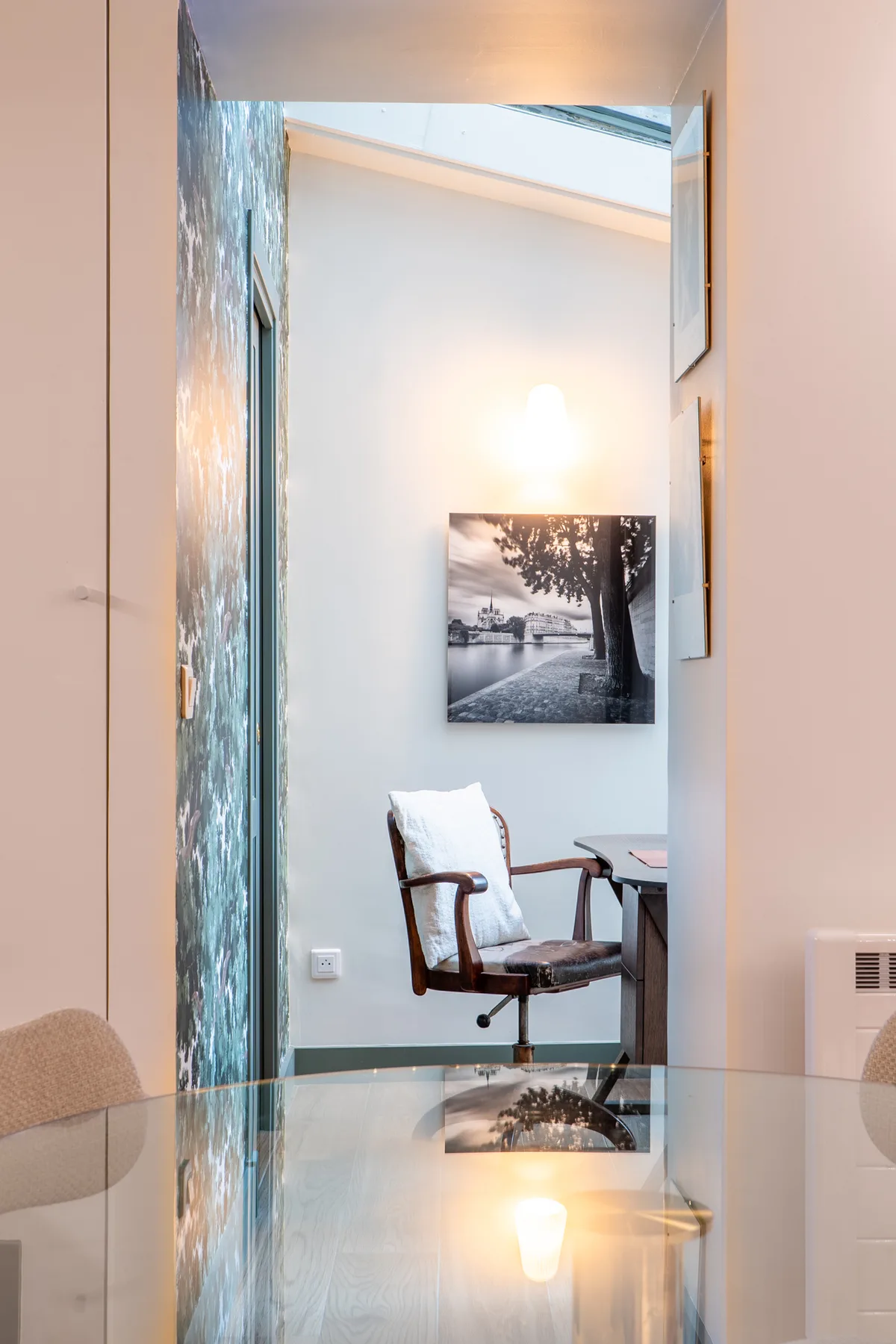 A desk and seating area is visible beyond a glass partition, with a framed landscape print.