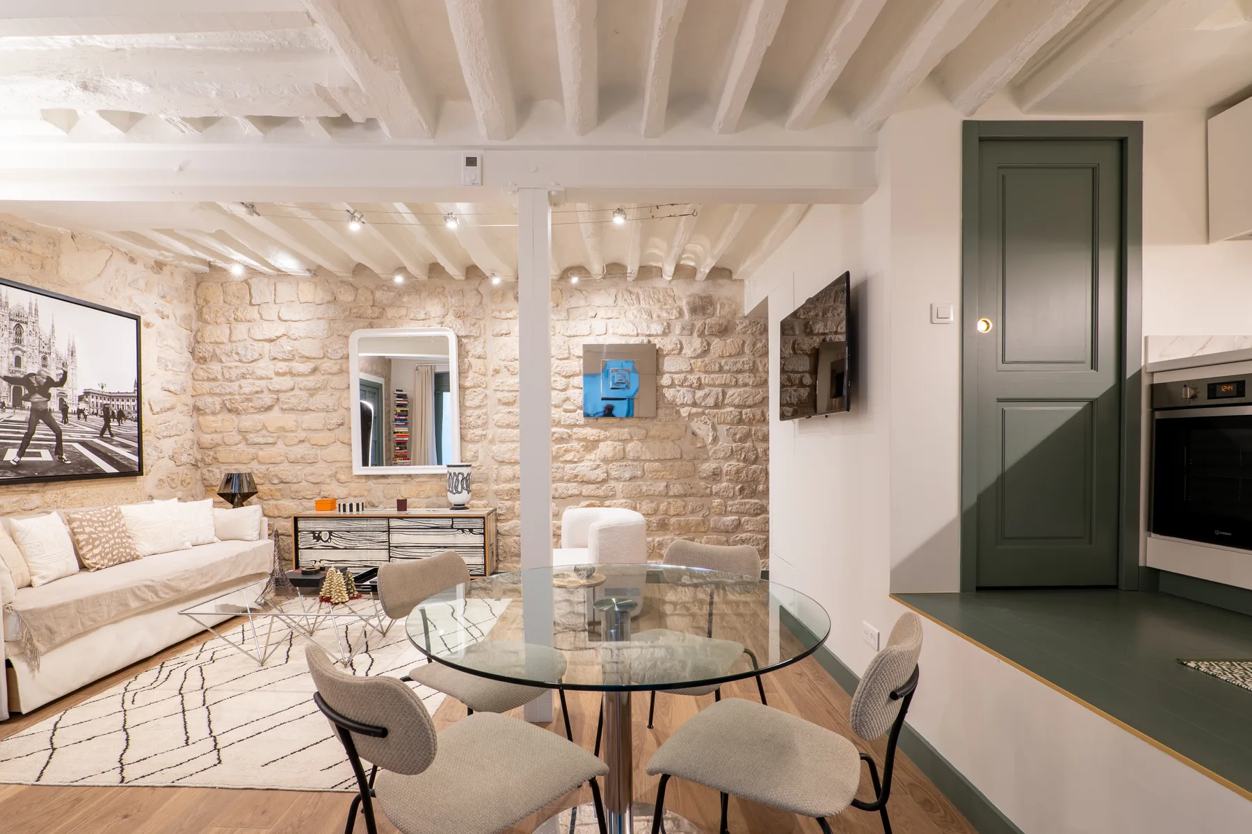 A bright living and dining room with stone walls and a glass dining table.